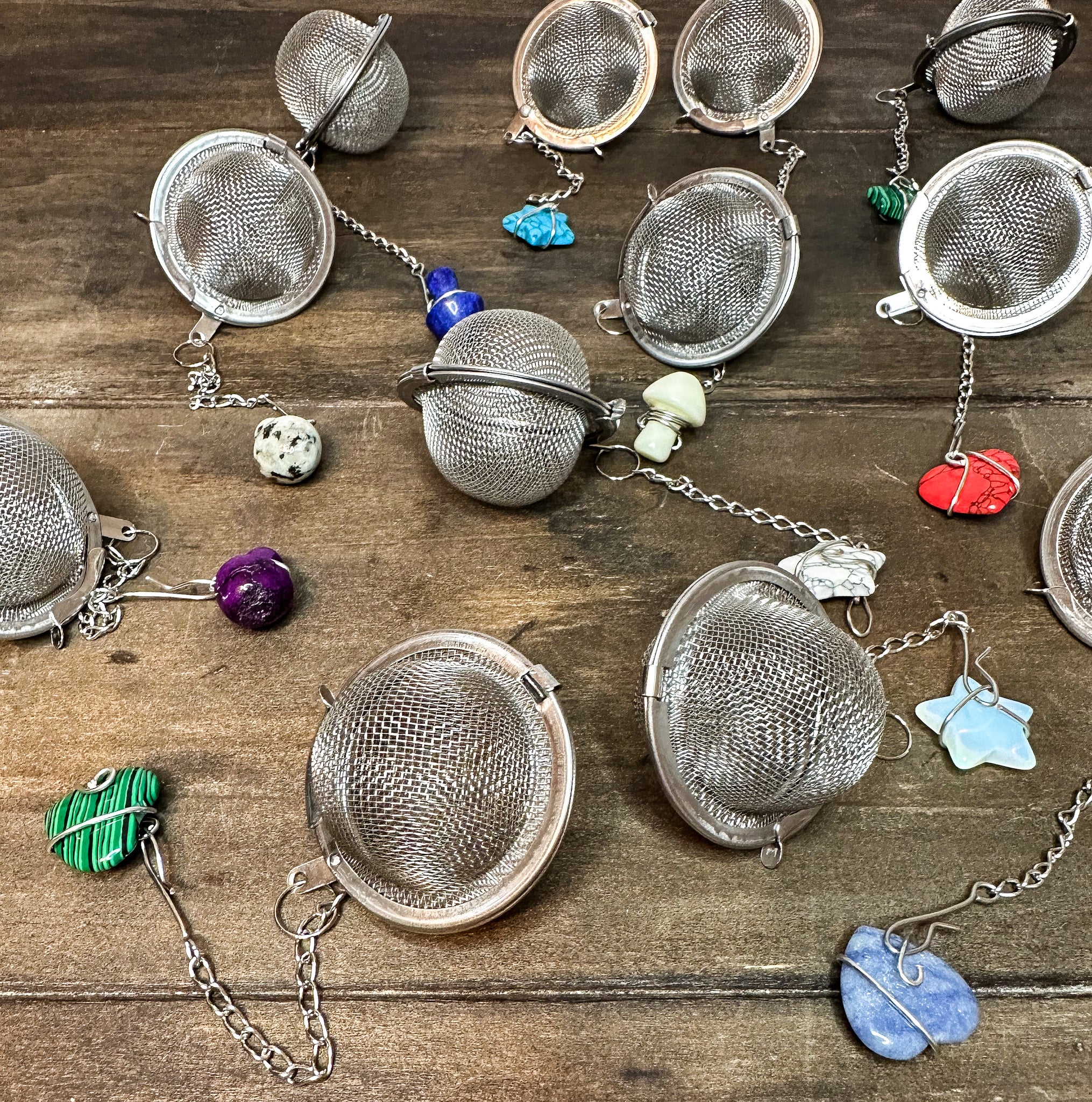 Several different tea ball infusers with crystals on the ends of the chains