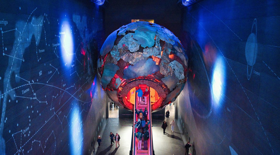 Large ethereal globe and people entering through escalator.
