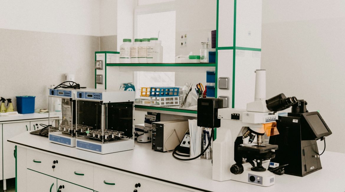 Medical lab with white lab bench, drawers, and multiple lab machines including a microscope.